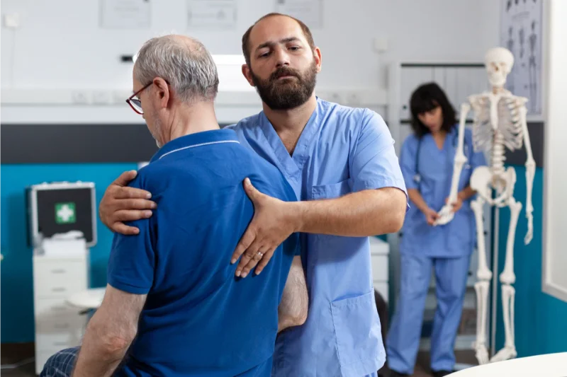Chiropractor examining patient's back and spine, skeletal model in background